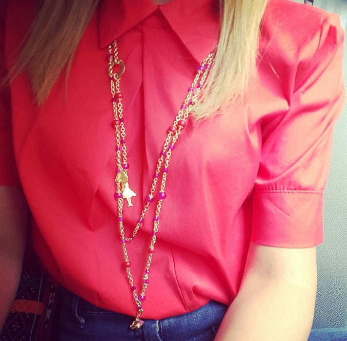 lady in red top wearing le carose long chain gold plated necklace with pink jewels and charms.