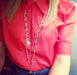 lady in red top wearing le carose long chain gold plated necklace with pink jewels and charms.