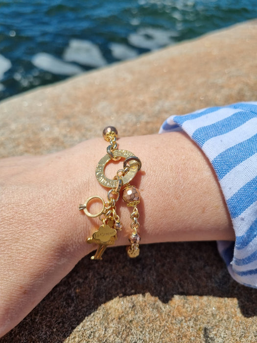 lady wearing gold charm bracelet with engagement ring and le carose charm. blue ocean background